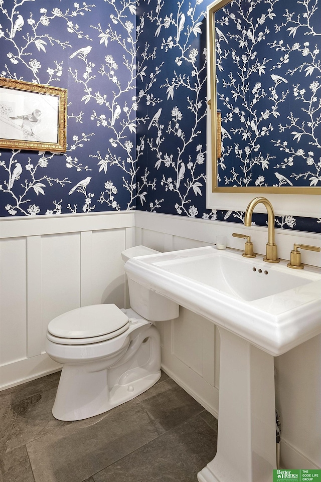 half bath with a wainscoted wall, toilet, and wallpapered walls