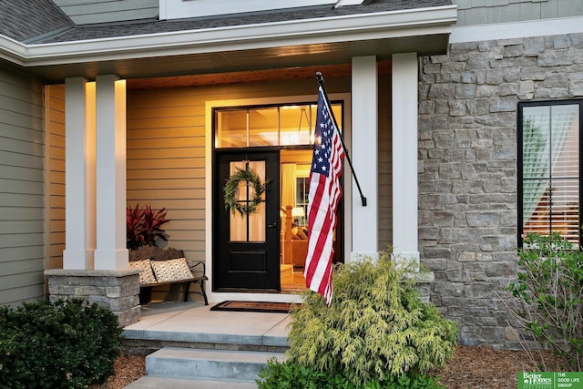 property entrance featuring roof with shingles, covered porch, and stone siding