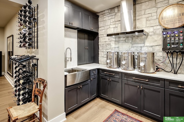 bar featuring wall chimney range hood, backsplash, light wood finished floors, and a sink