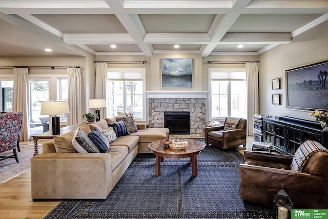 living area featuring beam ceiling, a stone fireplace, a wealth of natural light, and coffered ceiling