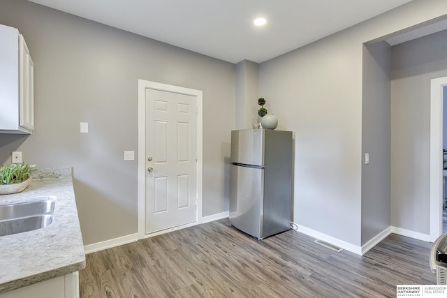 interior space featuring freestanding refrigerator, baseboards, light wood-type flooring, white cabinets, and a sink