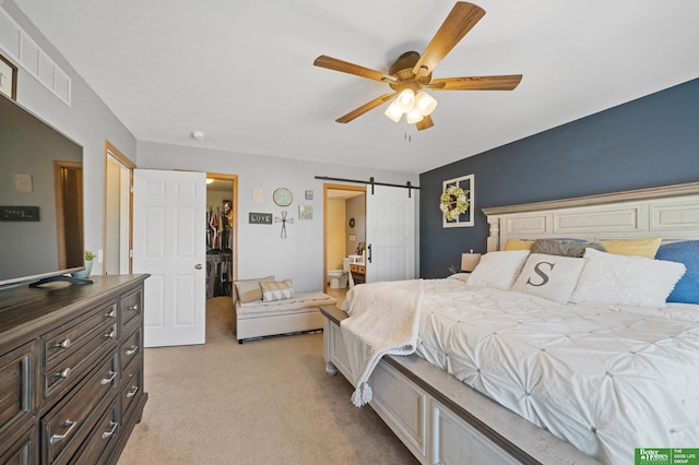 bedroom featuring visible vents, a walk in closet, light colored carpet, a barn door, and a ceiling fan