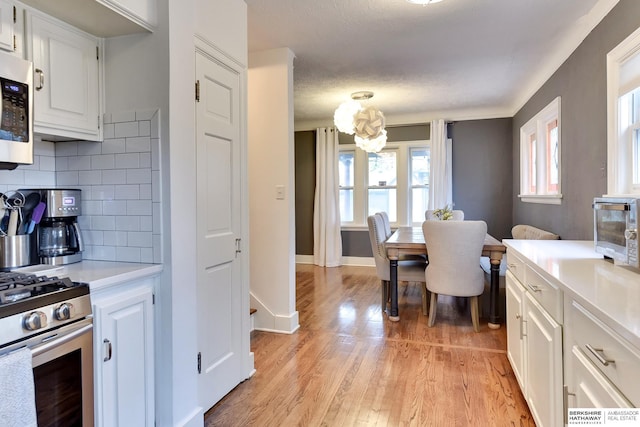 5117 Western Ave, Omaha, NE 68132 - kitchen with decorative backsplash, light wood-type flooring, light countertops, white cabinets, and stainless steel appliances