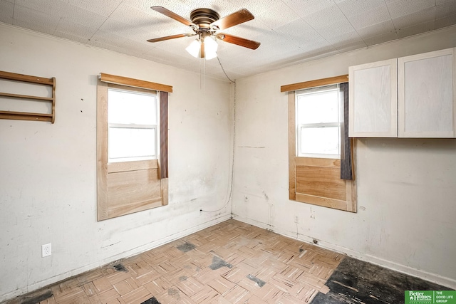empty room featuring baseboards, ceiling fan, and a wealth of natural light
