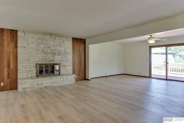 unfurnished living room featuring baseboards, a ceiling fan, a stone fireplace, and wood finished floors