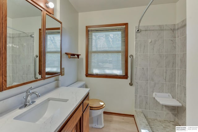 bathroom featuring toilet, baseboards, a tile shower, and vanity