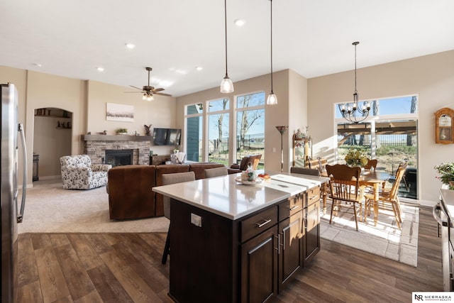 kitchen with a stone fireplace, ceiling fan with notable chandelier, freestanding refrigerator, a wealth of natural light, and dark wood-style floors