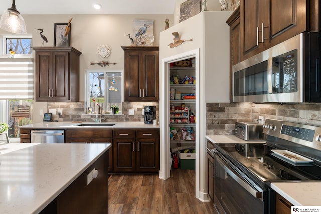 kitchen featuring a sink, appliances with stainless steel finishes, backsplash, and dark wood-style flooring