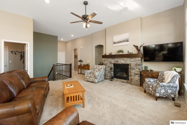 carpeted living room featuring arched walkways, ceiling fan, recessed lighting, and a stone fireplace