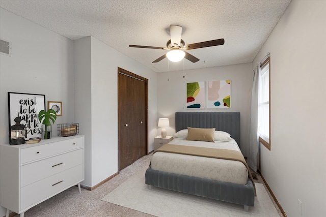 bedroom featuring ceiling fan, light carpet, a textured ceiling, baseboards, and a closet