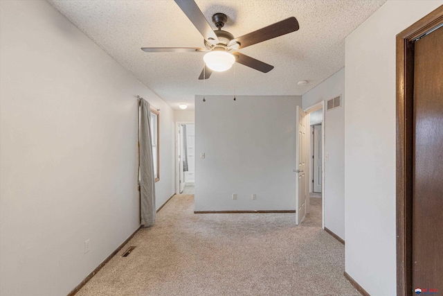 spare room with a ceiling fan, a textured ceiling, light colored carpet, visible vents, and baseboards