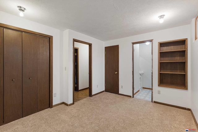unfurnished bedroom featuring light colored carpet, a textured ceiling, baseboards, and ensuite bathroom