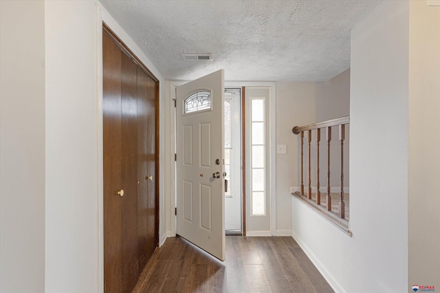 foyer featuring baseboards, dark wood-style floors, a textured ceiling, and visible vents