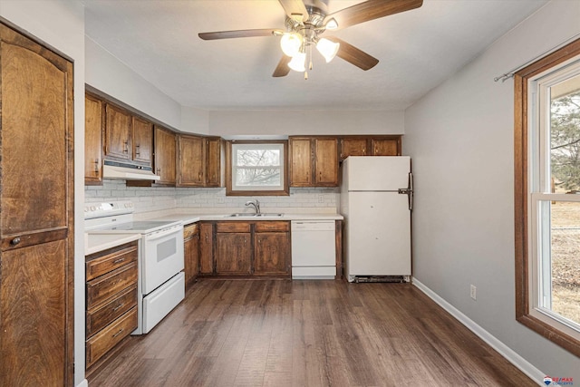 kitchen with dark wood-style flooring, white appliances, under cabinet range hood, tasteful backsplash, and a sink