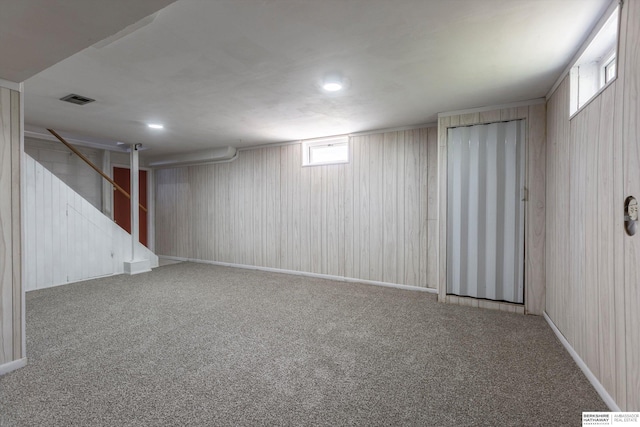 basement featuring stairs, wood walls, visible vents, and carpet