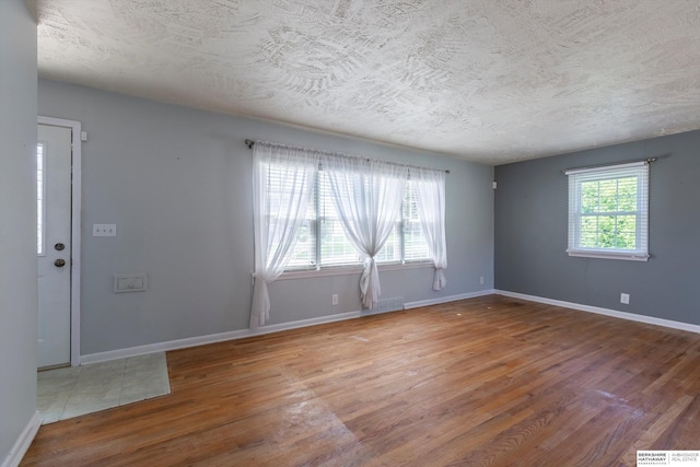 spare room with a textured ceiling, baseboards, and wood finished floors