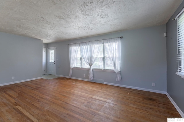 spare room featuring baseboards, a textured ceiling, wood finished floors, and visible vents