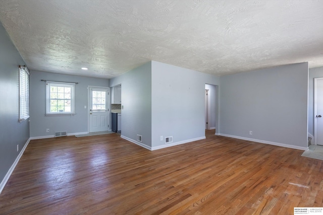 unfurnished living room featuring a textured ceiling, baseboards, wood finished floors, and visible vents