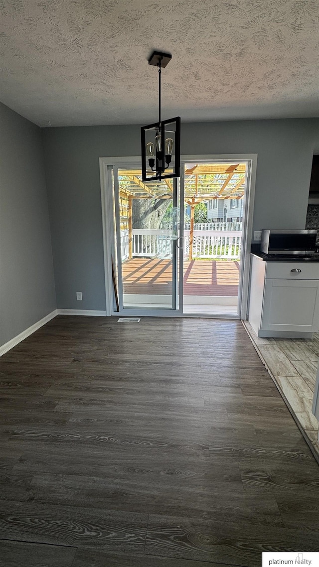 unfurnished dining area with an inviting chandelier, a textured ceiling, baseboards, and dark wood-style floors