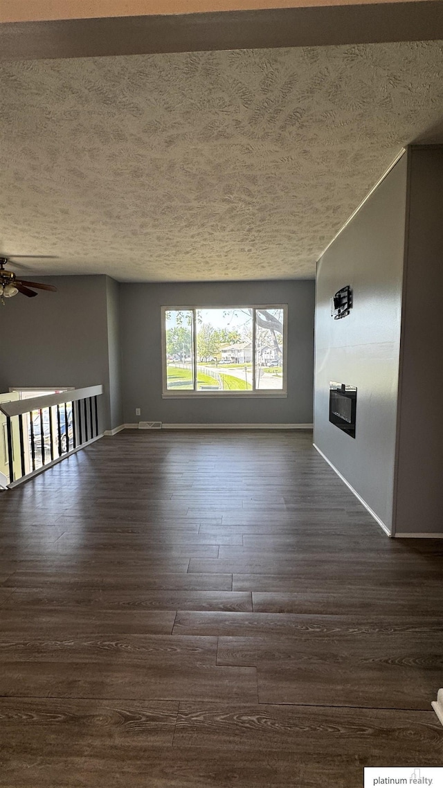 unfurnished living room featuring baseboards, a textured ceiling, and dark wood-style flooring
