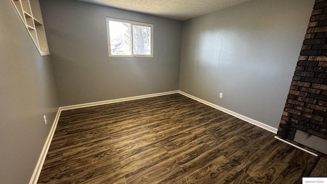 spare room featuring baseboards, dark wood-style flooring, and a textured ceiling