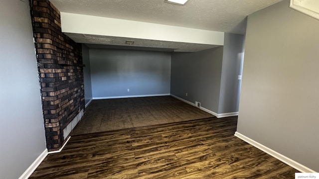 finished below grade area with dark wood-style flooring, a textured ceiling, visible vents, and baseboards