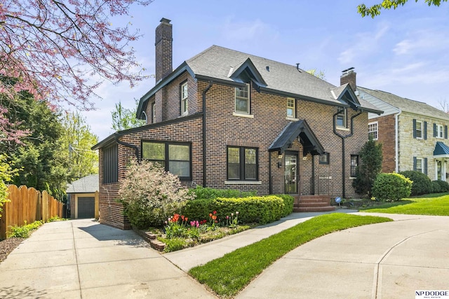 view of front of home featuring fence, a detached garage, a chimney, and brick siding