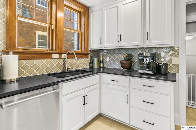 kitchen featuring white cabinets, a sink, dark stone counters, backsplash, and stainless steel dishwasher