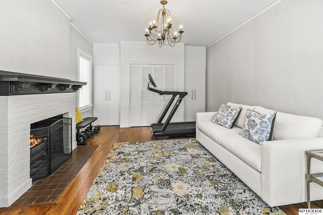 living room with crown molding, a chandelier, a brick fireplace, and wood finished floors