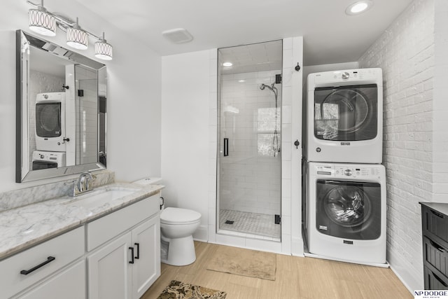 bathroom with vanity, stacked washer and clothes dryer, wood finished floors, toilet, and a shower stall