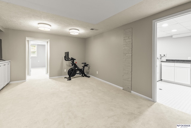 exercise area featuring a textured ceiling, baseboards, visible vents, and light carpet