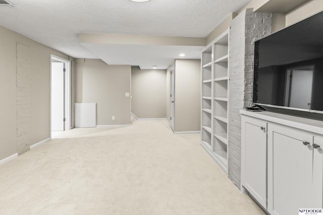 finished below grade area featuring built in shelves, baseboards, light carpet, and a textured ceiling