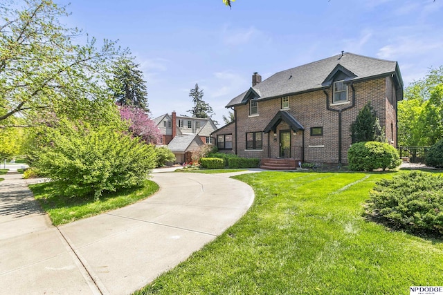 tudor house with a chimney, brick siding, and a front yard