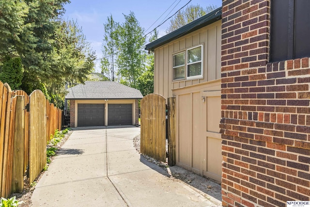 view of side of home with fence, brick siding, a gate, board and batten siding, and a detached garage