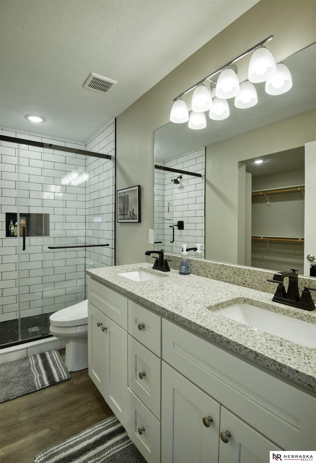 full bath featuring wood finished floors, double vanity, a sink, and a stall shower