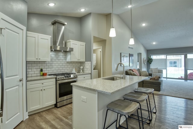 kitchen with light stone countertops, open floor plan, wall chimney range hood, a sink, and gas stove