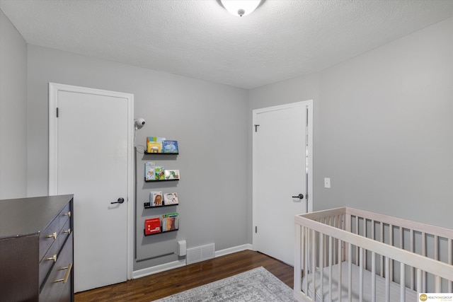 bedroom with visible vents, a textured ceiling, dark wood finished floors, and a nursery area