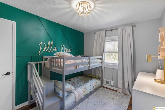 bedroom with a textured ceiling, a notable chandelier, wood finished floors, and visible vents