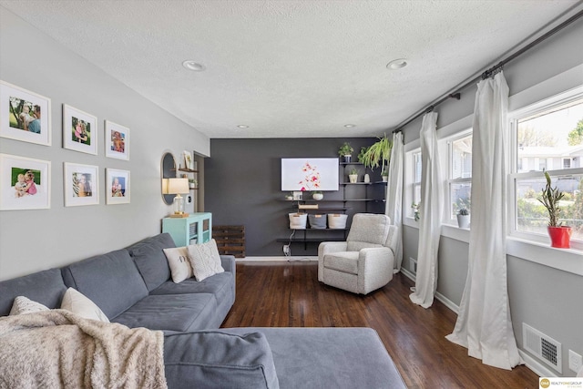 living area featuring visible vents, baseboards, a textured ceiling, and wood finished floors
