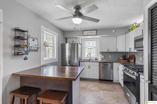 kitchen featuring decorative backsplash, wooden counters, a sink, stainless steel appliances, and white cabinetry