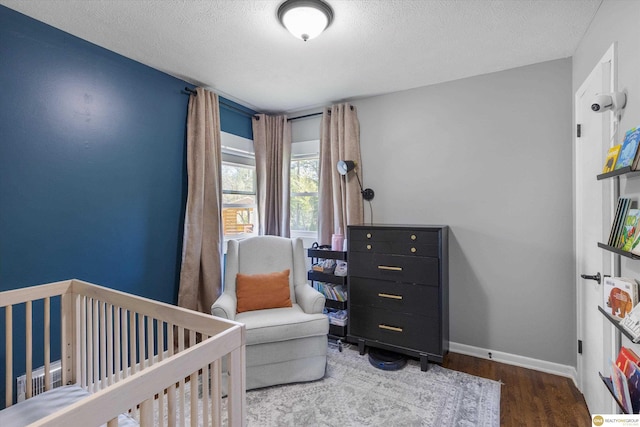 bedroom with a textured ceiling, baseboards, a nursery area, and wood finished floors