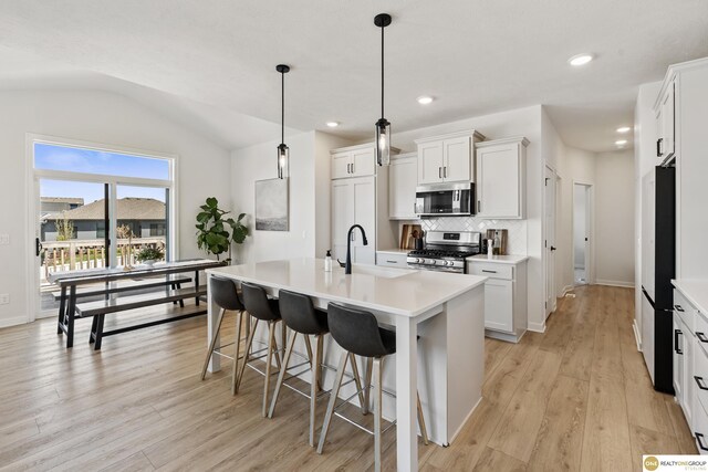 kitchen featuring a sink, stainless steel appliances, decorative backsplash, lofted ceiling, and light wood-type flooring