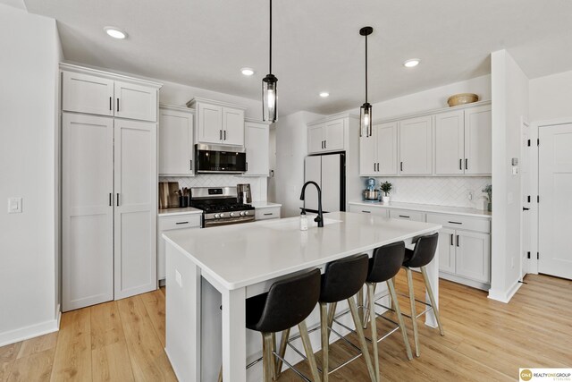 kitchen with light countertops, appliances with stainless steel finishes, decorative backsplash, and light wood-style flooring