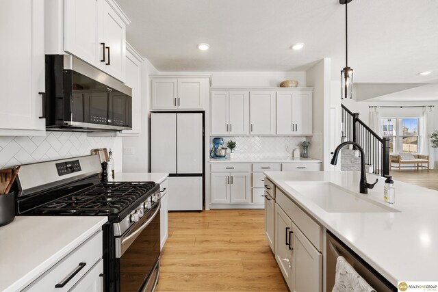 kitchen featuring appliances with stainless steel finishes, a sink, light countertops, light wood-style floors, and white cabinetry