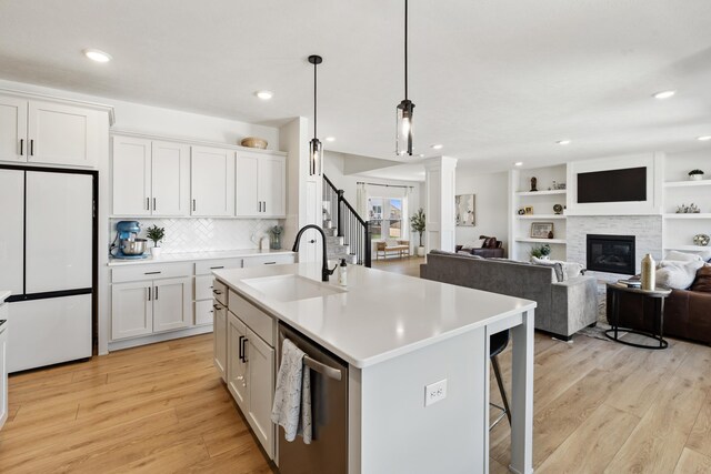 kitchen featuring dishwasher, a sink, light wood finished floors, white fridge, and white cabinetry