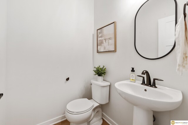 half bathroom with baseboards, a sink, and toilet