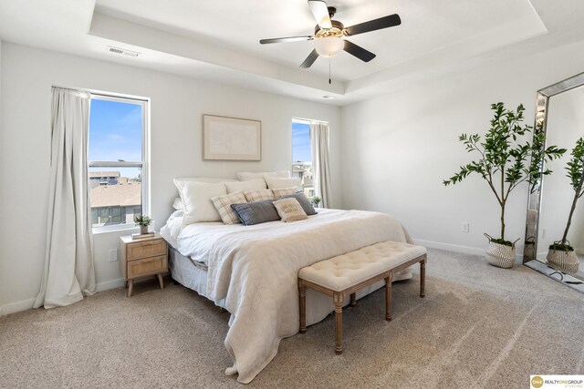 bedroom featuring a tray ceiling, visible vents, light carpet, and baseboards