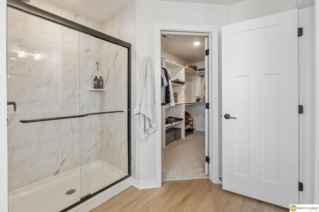bathroom with baseboards, a spacious closet, a shower stall, and wood finished floors