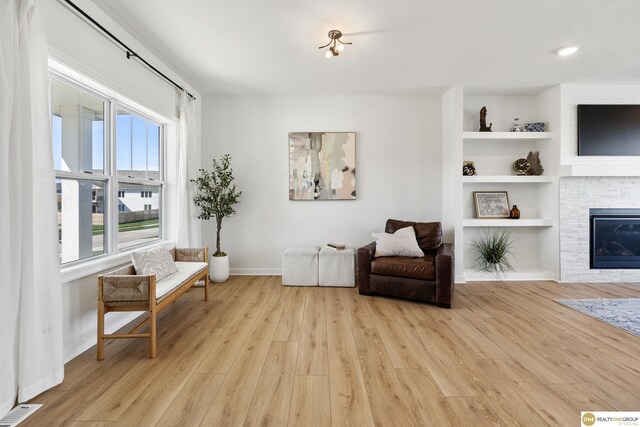 sitting room with visible vents, a glass covered fireplace, light wood-style floors, baseboards, and built in shelves