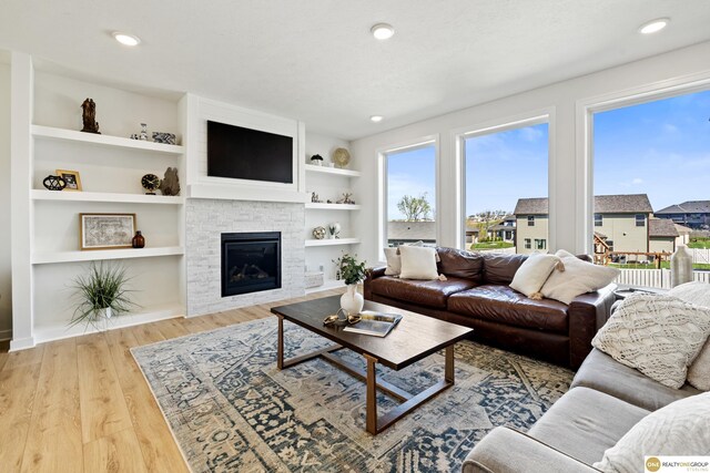 living area with recessed lighting, a glass covered fireplace, wood finished floors, and built in shelves